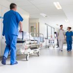 Male nurse pushing stretcher gurney bed in hospital corridor with doctors & senior female patient